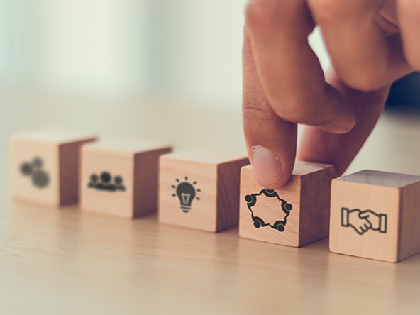 Hand reaching down towards wooden blocks showing icons such as shaking hands, holding hands, lightbulb